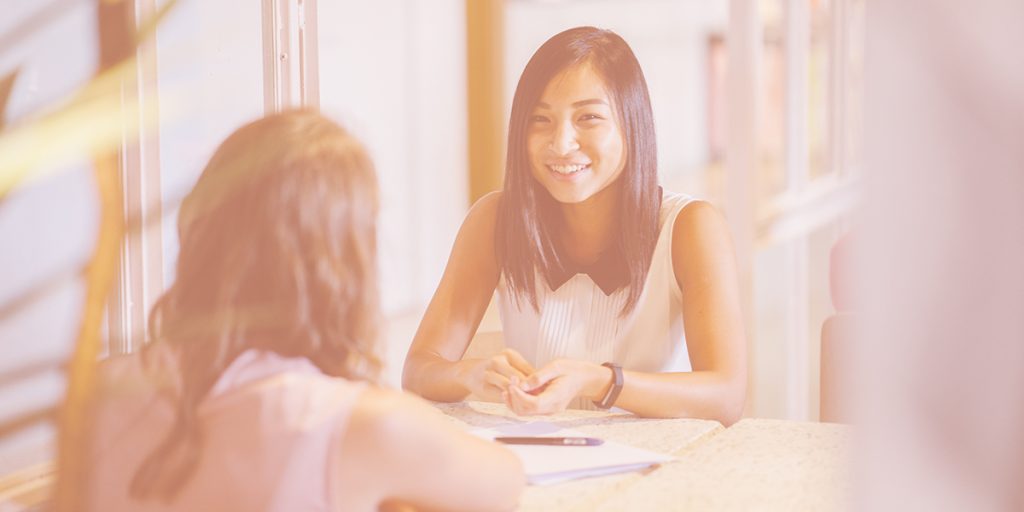 two young women sitting across from each other at a table one with her back to the camera and one smiling
