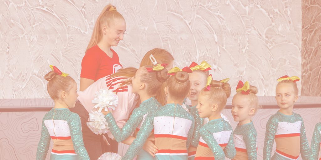 a group on young cheerleaders with their coach, smiling and laughing