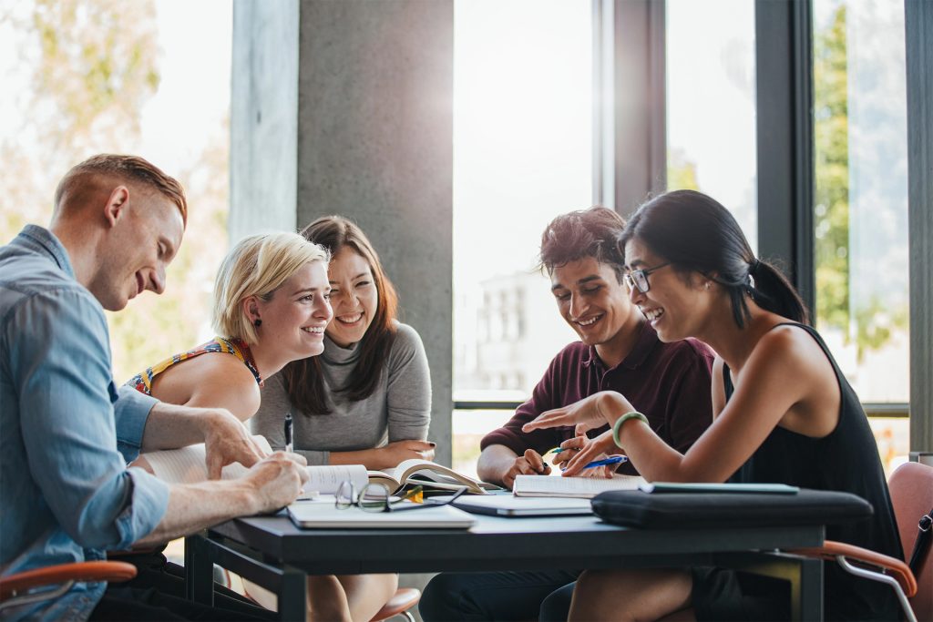 a group of people sitting at a table talking and laughing with homework in front of them
