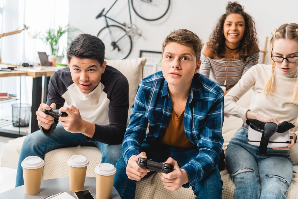 four teens playing video games on a couch